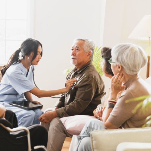 happiness Cheerful elderly woman and men talking with female caregiver nurse doctor having health checking consult at living area,Caretakers with senior couple sitting in living room at nursing home
